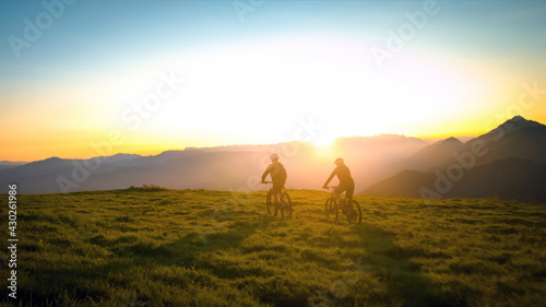 Mother and daughter cycling uphill with mountain bikes at a sunset.