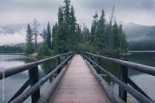 Wooden bridge leading to a small island in the background. Pyramid Lake in Canadian Rockies. Misty, rainy evening in Jasper National Park, Alberta, Canada.