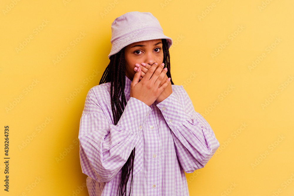 Young african american woman isolated on yellow background covering mouth with hands looking worried. Young african american woman isolated on yellow background covering mouth with hands looking worried.