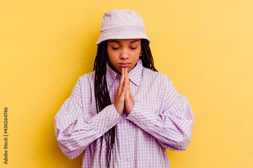 Young african american woman isolated on yellow background praying, showing devotion, religious person looking for divine inspiration.