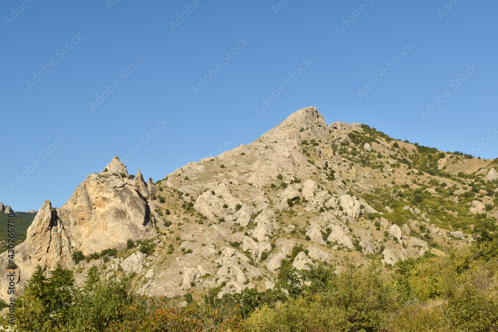 landscape with a small mountain and dense greenery at the base against a clear blue sky shot in summer
