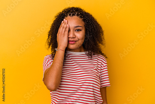 Young african american woman isolated on yellow background having fun covering half of face with palm.