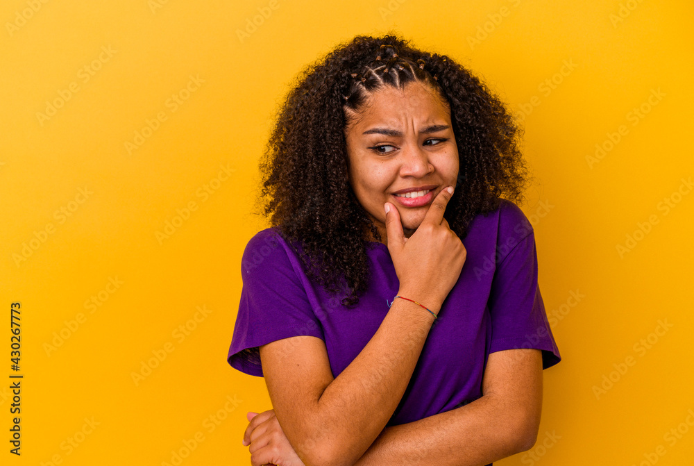 Young african american woman isolated on yellow background touching back of head, thinking and making a choice. Young african american woman isolated on yellow background touching back of head, thinking and making a choice.