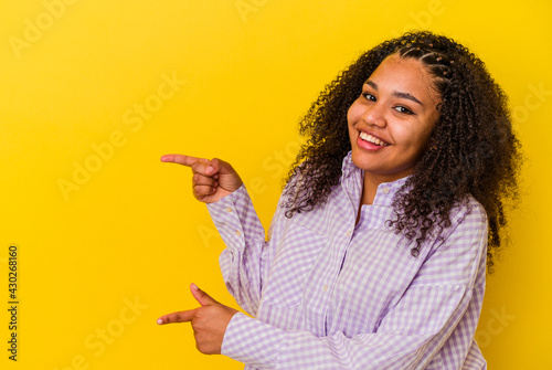 Young african american woman isolated on yellow background excited pointing with forefingers away.