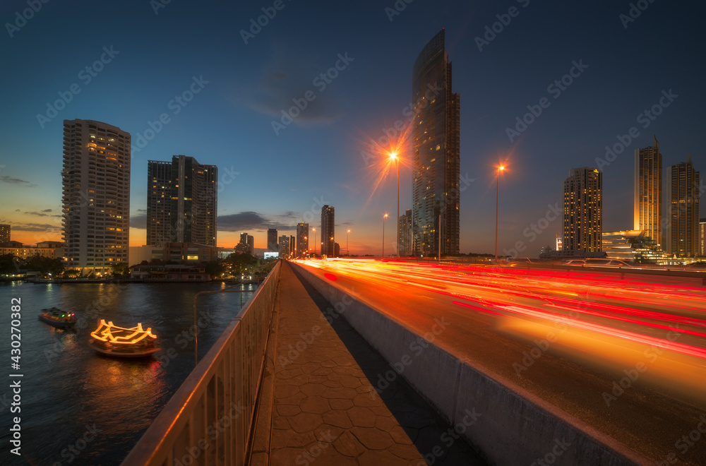 Skyscrapers and Traffic Light Trails on Taksin Bridge Crossing Chao Phraya River in Bangkok, Thailand at Twilight