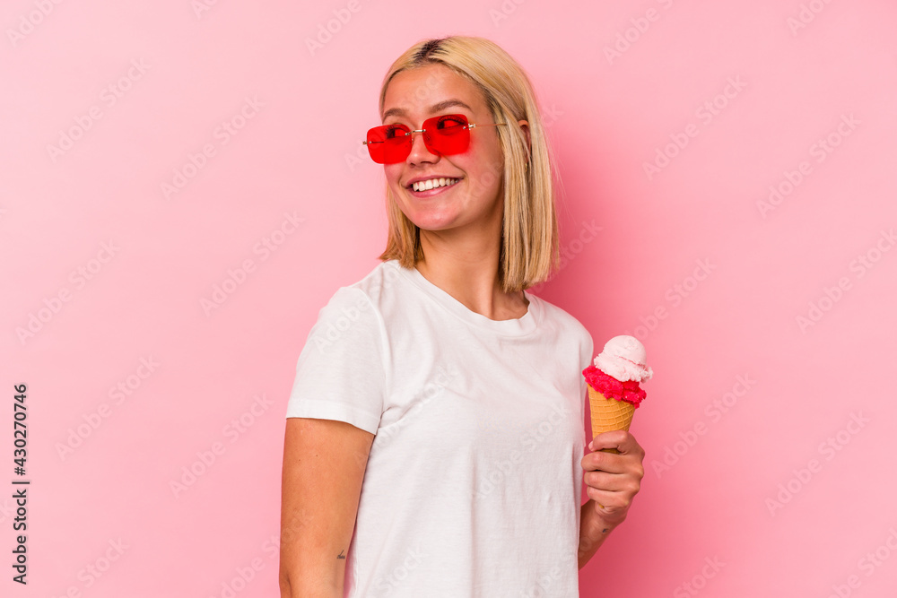 Young venezuelan woman eating an ice cream isolated on pink background looks aside smiling, cheerful and pleasant. Young venezuelan woman eating an ice cream isolated on pink background looks aside smiling, cheerful and pleasant.