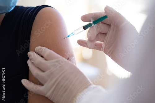 Coronavirus vaccination  doctor injecting a patient  getting first shot of covid vaccine in arm muscle. Medical doctor in protective suit and mask  process of immunization against covid-19