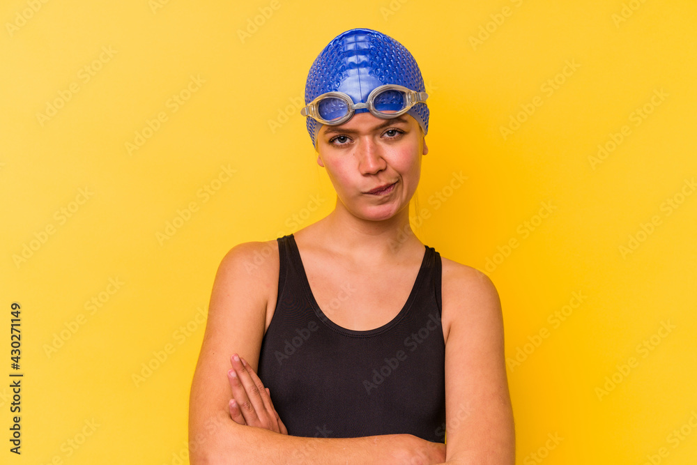Young swimmer venezuelan woman isolated on yellow background frowning face in displeasure, keeps arms folded.