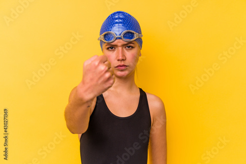 Young swimmer venezuelan woman isolated on yellow background showing fist to camera, aggressive facial expression.