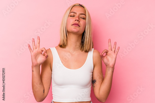 Young venezuelan woman isolated on pink background relaxes after hard working day, she is performing yoga. © Asier