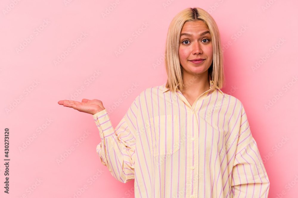 Young venezuelan woman isolated on pink background showing a copy space on a palm and holding another hand on waist. Young venezuelan woman isolated on pink background showing a copy space on a palm and holding another hand on waist.