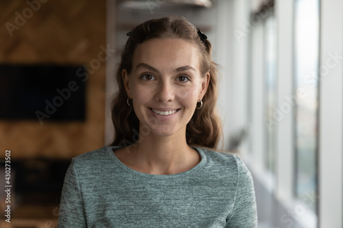 Headshot portrait of smiling young Caucasian woman pose in modern office during work day. Profile close up picture of happy millennial female employee or worker show leadership success at workplace.