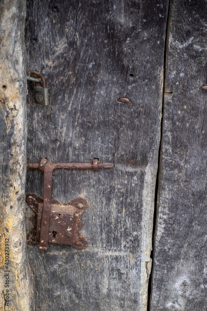 close up of an old and deteriorated wooden door with a rusty metal latch and a padlock, rural texture, vertical close up of an old and deteriorated wooden door with a rusty metal latch and a padlock, rural texture, vertical