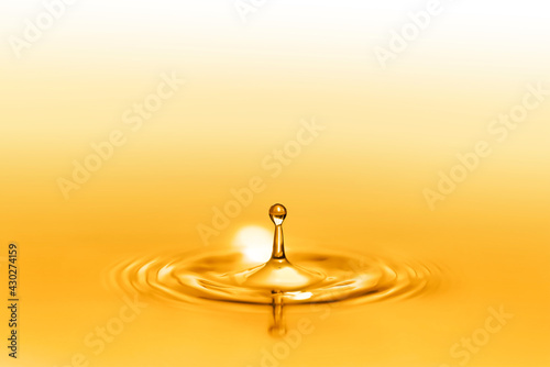 Close up on drop splash of a healthy extra-virgin oil full of oligo elements and vitamins creating circular waves by falling down on the liquid and seamless pure surface shining with golden reflects.