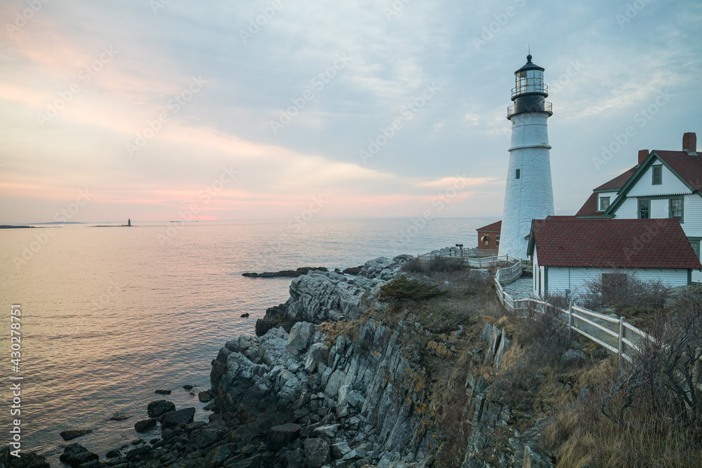 The morning sunrise over the ocean coast of Maine behind Portland Head Lighthouse.