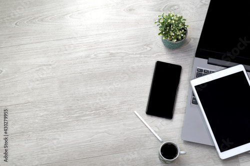Wood office desk with computer, mobile phone, tablet, tablet pen, coffee and plant