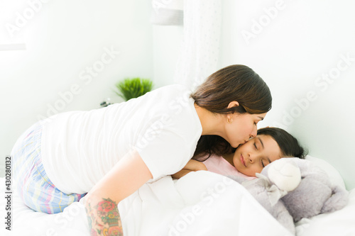 Affectionate mother tucking her kid in bed