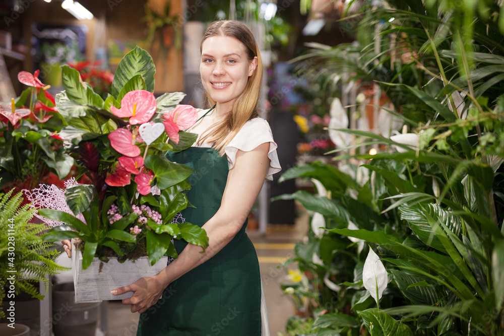 Cheerful woman florist holding pot with a flower in the gardening market. High quality photo