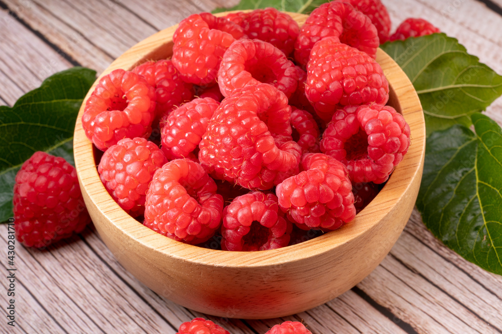 Raspberry fruit on wooden bowl in Wooden background, Raspberries with leaves on Wooden background. Raspberry fruit on wooden bowl in Wooden background, Raspberries with leaves on Wooden background.