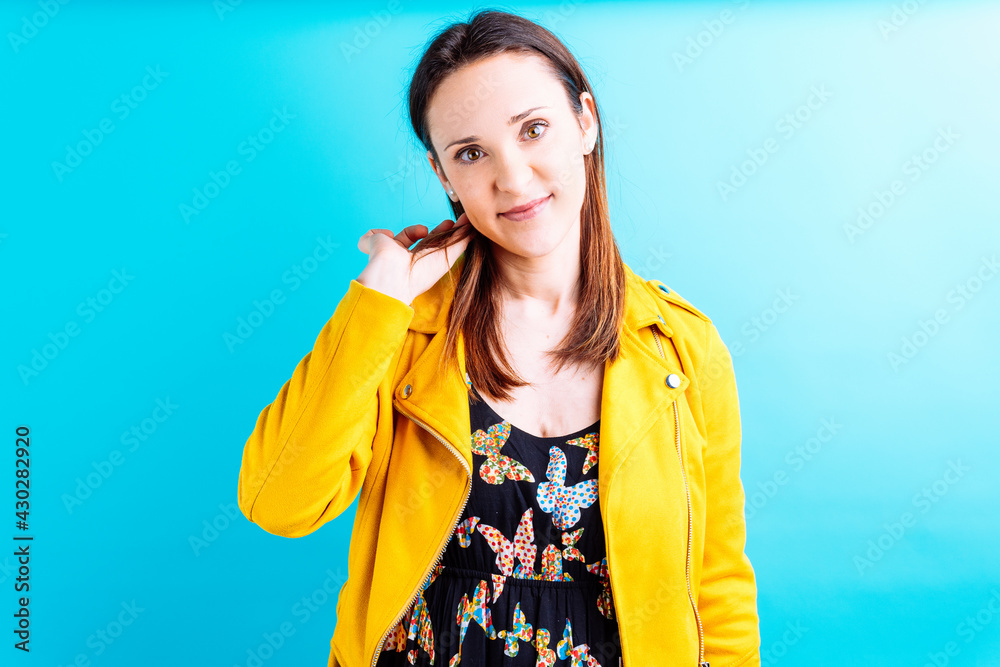 beautiful young woman in yellow jacket on blue background tucking her hair behind her ear. flirt concept beautiful young woman in yellow jacket on blue background tucking her hair behind her ear. flirt concept