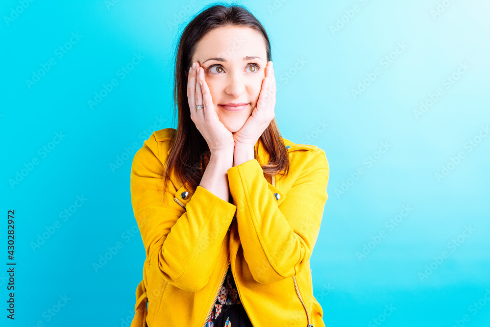 beautiful young woman in yellow jacket with hands on surprised face