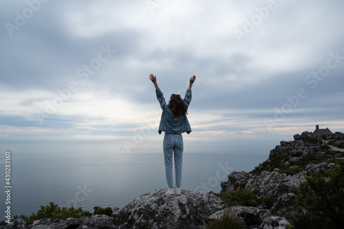 Woman in blue jeans raising hands against cloudy sky and calm ocean