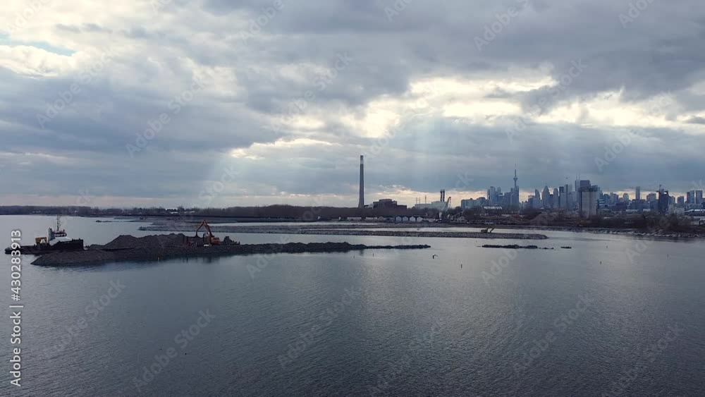 Heavy equipment building breakwater from rocks with near waterfront and Toronto skyline; aerial crane up Heavy equipment building breakwater from rocks with near waterfront and Toronto skyline; aerial crane up