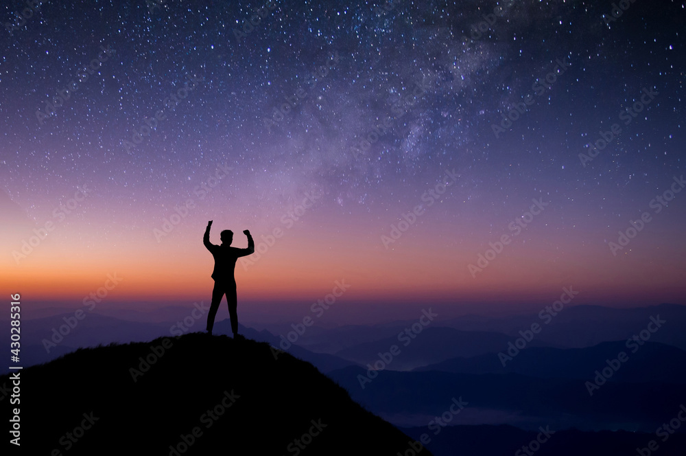 Young traveler standing and looking view star, Milky Way on top of mountain. He strong confidence and open arms under the night sky. He enjoyed traveling and was successful when he reached the summit.