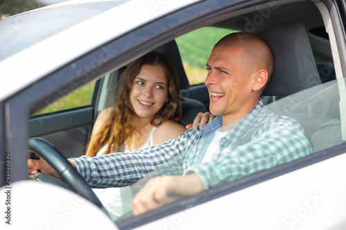 Portrait of cheerful young man driving car with his girlfriend in front passenger seat. Road trip and dating concept © JackF