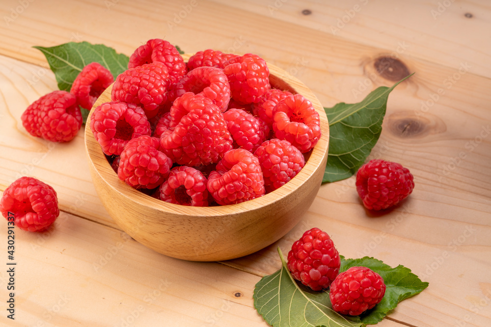 Raspberry fruit in tiny wooden bowl on Wooden background, Raspberries with leaves on Wooden background. Raspberry fruit in tiny wooden bowl on Wooden background, Raspberries with leaves on Wooden background.