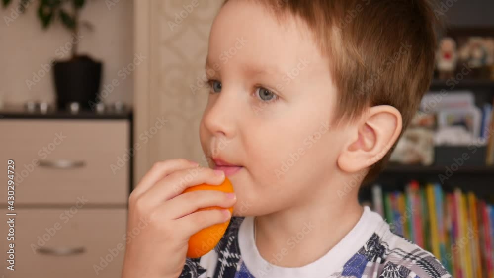 A happy little boy licks a half of a ripe orange and smiles close-up A happy little boy licks a half of a ripe orange and smiles close-up