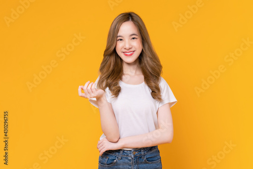 Studio shot of cheerful beautiful Asian woman in white t-shirt and stand on yellow background.