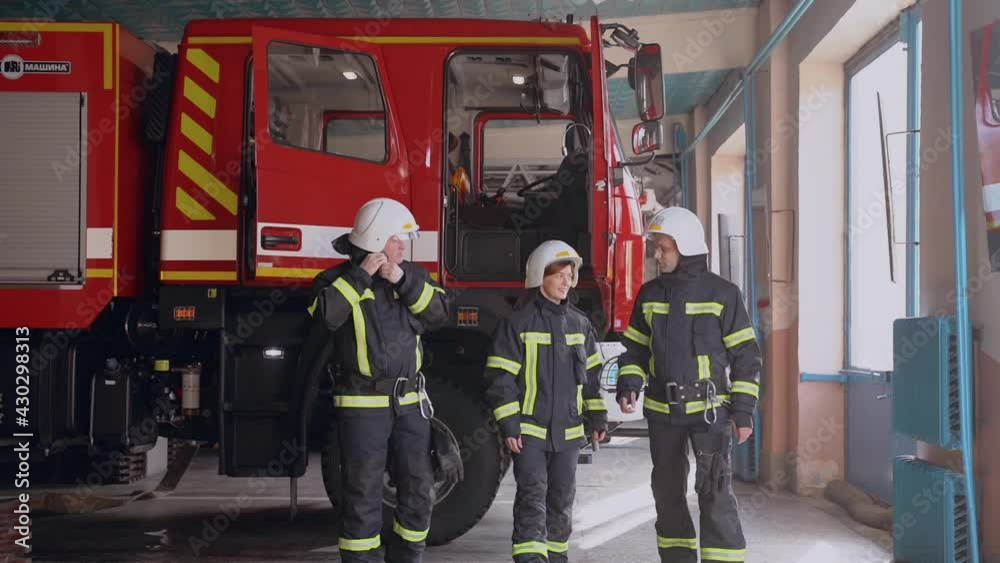 Three firefighter gear standing at the fire truck at the station Three firefighter gear standing at the fire truck at the station