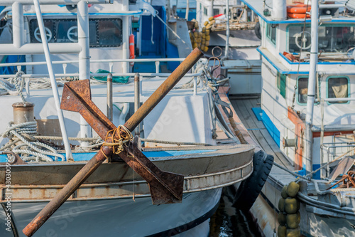 Large rusty iron anchor on bow of docked boat.