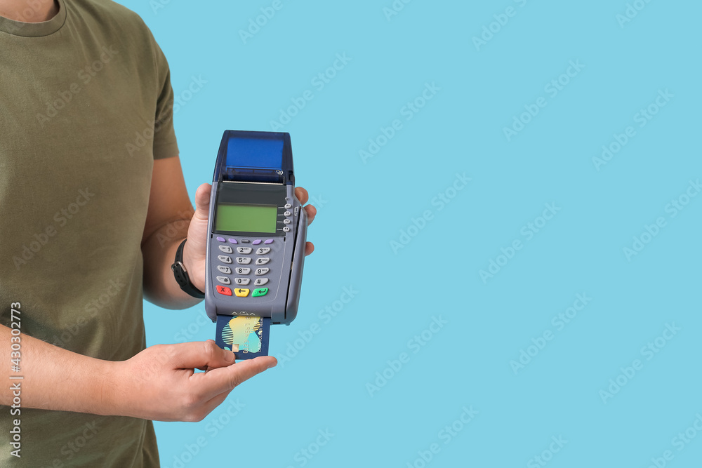 Young man with payment terminal and credit card on color background Young man with payment terminal and credit card on color background