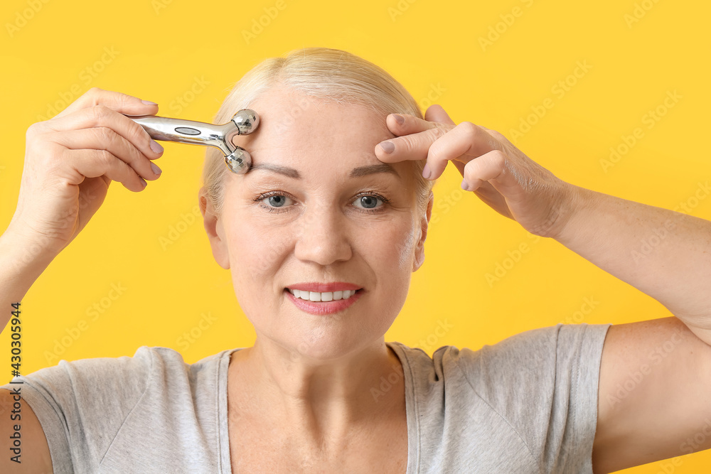 Mature woman with facial massage tool on color background Mature woman with facial massage tool on color background