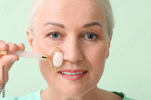 Mature woman with facial massage tool on color background