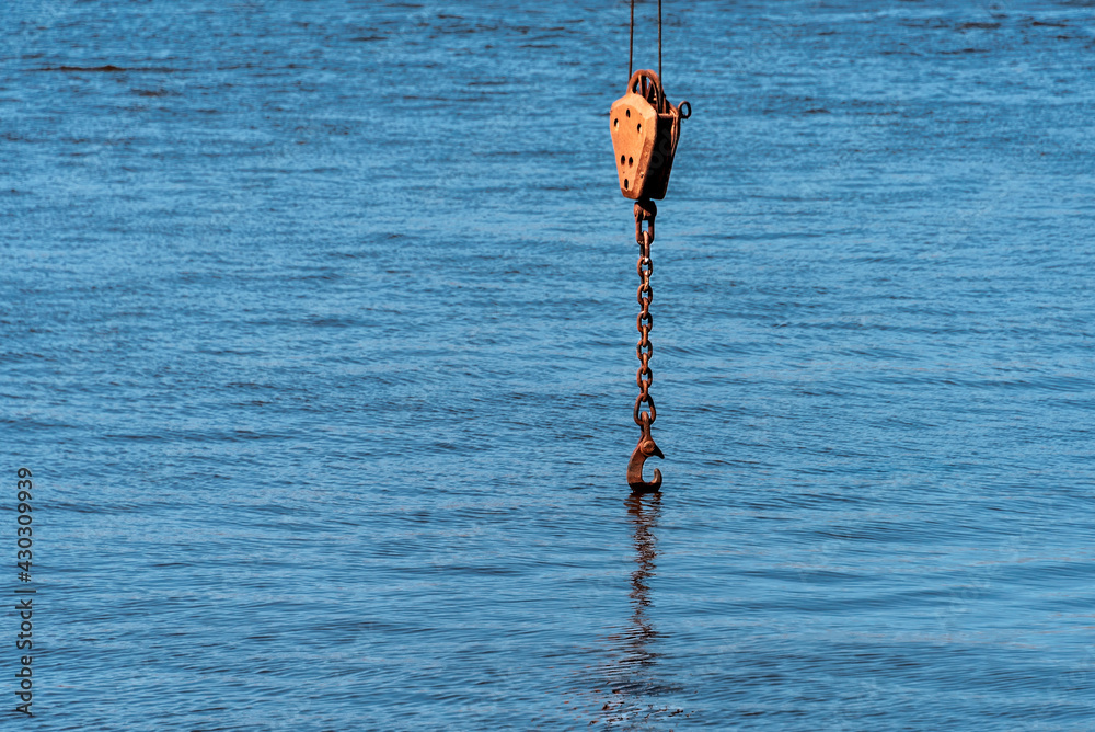 The arrow of a river crane with a chain and a hook lowered into the water against the background of the water. The arrow of a river crane with a chain and a hook lowered into the water against the background of the water.