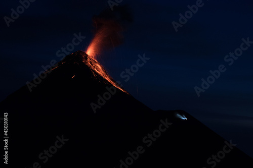 Impressive eruption with incandescent material and lava from the Fuego volcano seen from the Acatenango Volcano camp area at dusk with the dim light of a flashlight near the base.