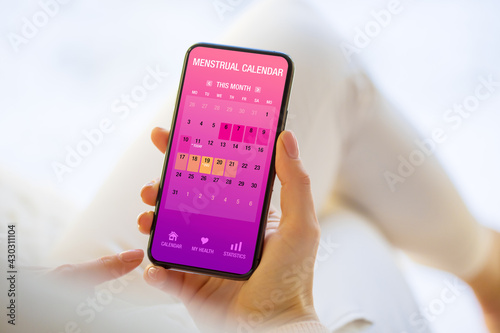 Woman tracking periods by using menstrual calendar app on phone photo