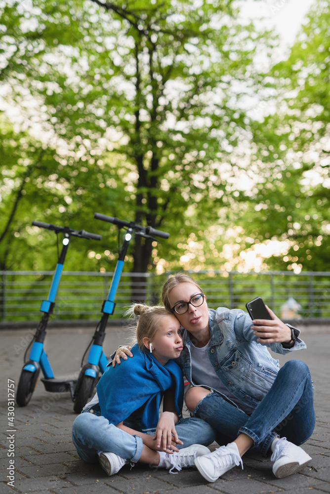 Happy mother and daughter taking selfie while electric scooters ride Happy mother and daughter taking selfie while electric scooters ride