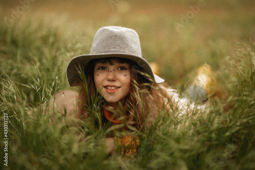 girl in a hat lies in green spring grass and smiles