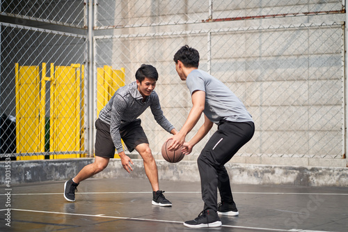 two young asian men playing basketball outdoors