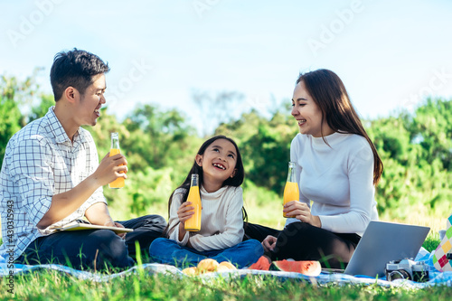 happy Asian family is having picnic in garden and drinking Orange juice in bottle with their daughters on holiday happily. © jumlongch