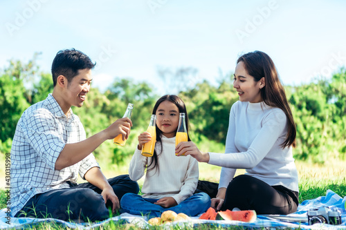 happy Asian family is having picnic in garden and drinking Orange juice in bottle with their daughters on holiday happily. © jumlongch