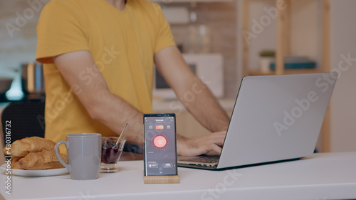 Man working from home with automation lighting system using voice controlled on smartphone turning on the light. Smart speaker gadget responds to commands, person controlling electricity effiency photo