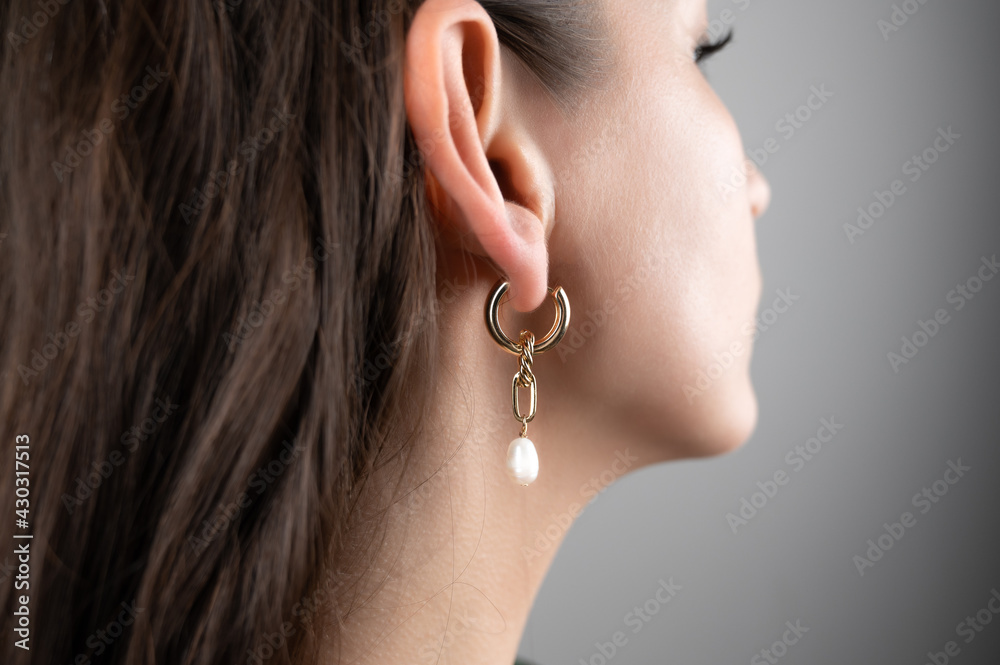 Young woman demonstrating stylish golden earrings, cropped view. Fashionable jewelry. 