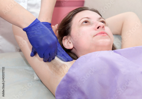 Depilation female armpit with liquid sugar paste. Hand of cosmetologist applying wax paste on armpit.