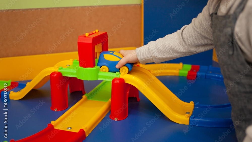 A two-year-old girl plays with toys in the playroom. Development Centre, Kindergarten Baby plays with plastic typewriter, road designer, multi-colored race track the car rolls on the road
