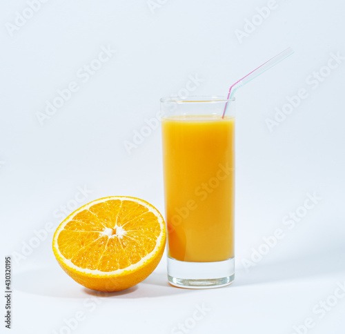 A glass of fresh orange juice, a straw, half of an orange, white background